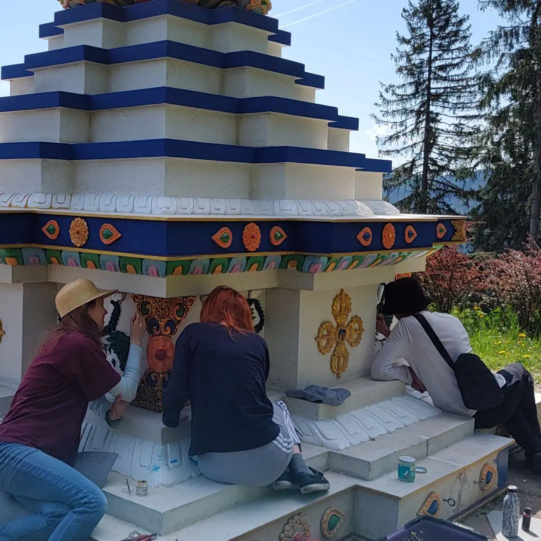 stupa-painting Dharma students volunteering to paint the stupa at Dzokden Kalap in Austria. They are adding blue paint and painting the details.